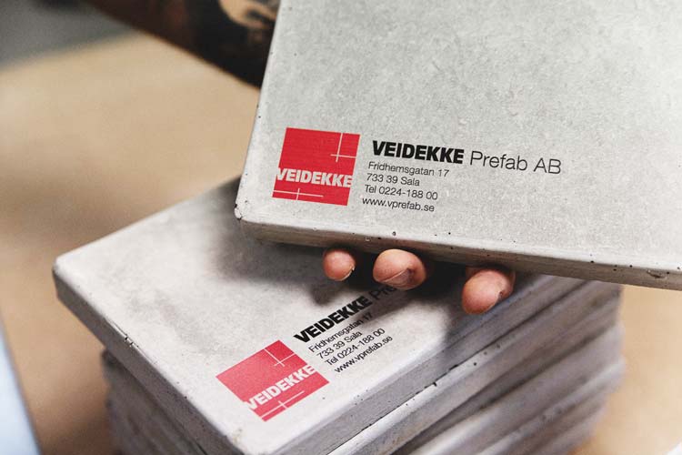 En person håller en betongbit i handen. På betongbiten är Veidekkes uppgifter printade.